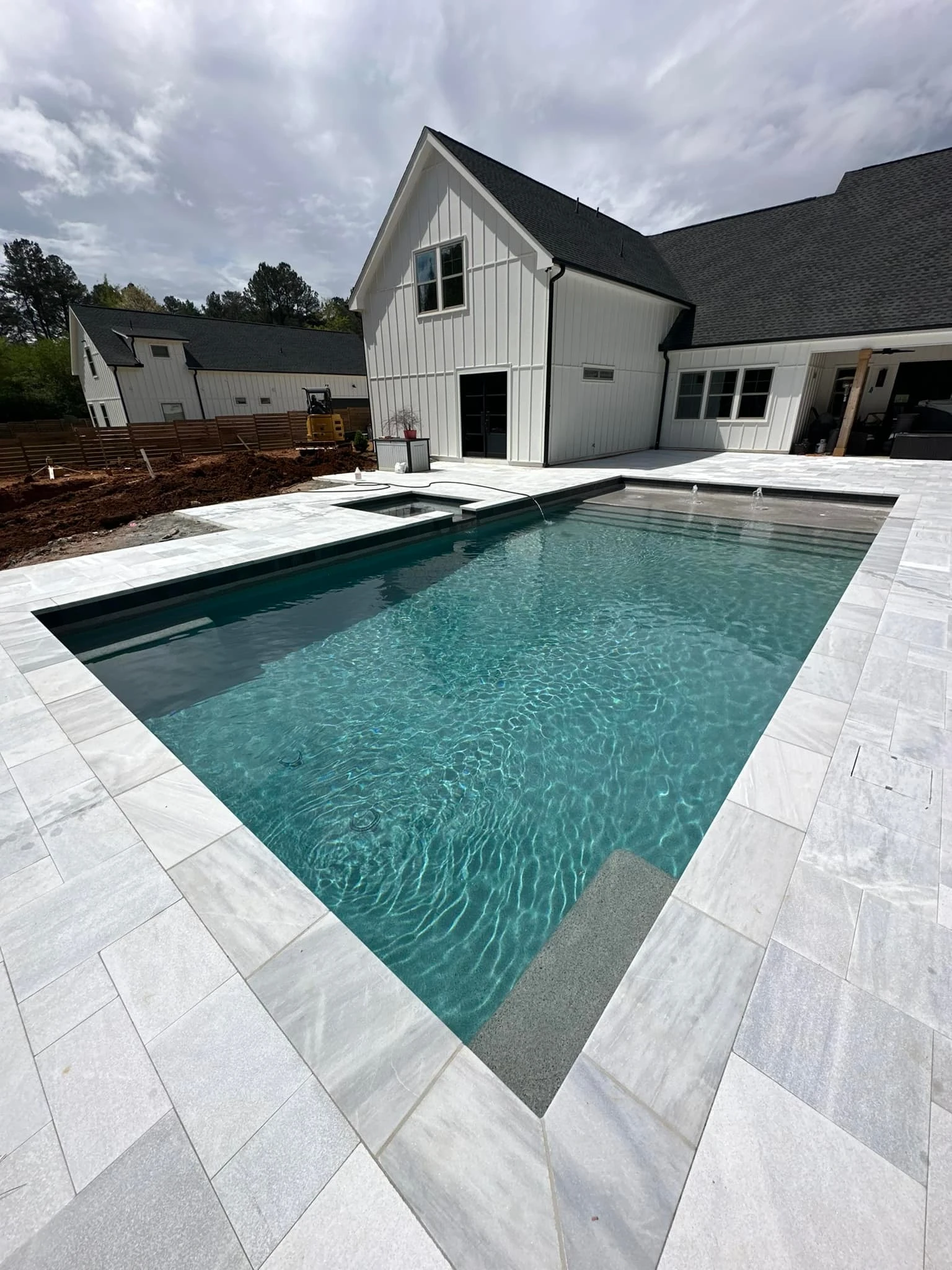 Completed backyard pool with travertine deck and surrounding landscaping on a residential lot in Alpharetta, GA