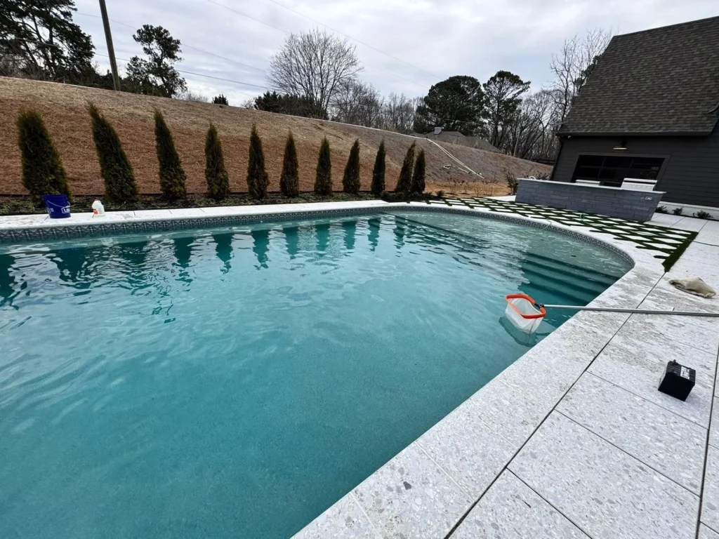 Rectangular pool with raised sheer-descent spa wall, white French-pattern travertine deck, winter graded slope and arborvitae row — custom pool design and installation in Cumming, GA by Primetime Pools.