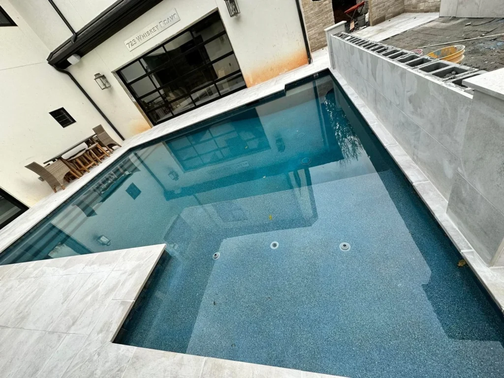 Narrow courtyard plunge pool with blue pebble finish mid-startup, street address sign visible on house wall — custom pool design and installation in Forsyth County, GA by Primetime Pools.