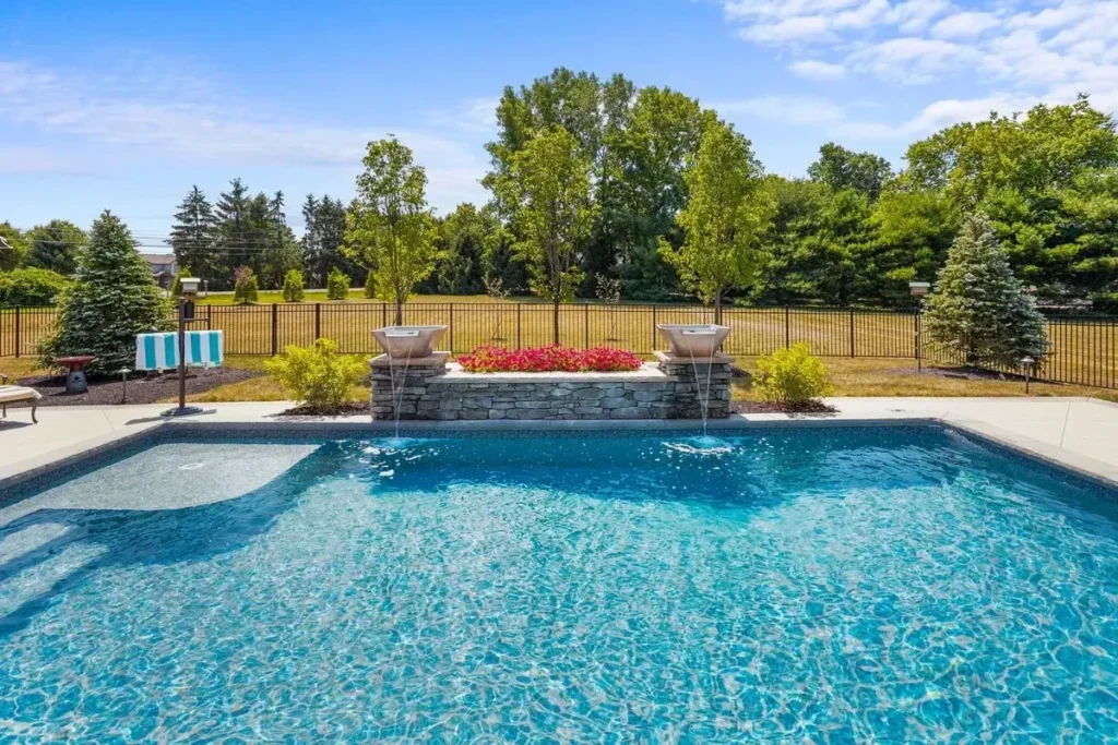 Wide eye-level across rectangular pool to stacked-stone raised planter wall with red-barberry strip and twin stone column piers with… — custom pool design and installation in Milton, GA by Primetime Pools.