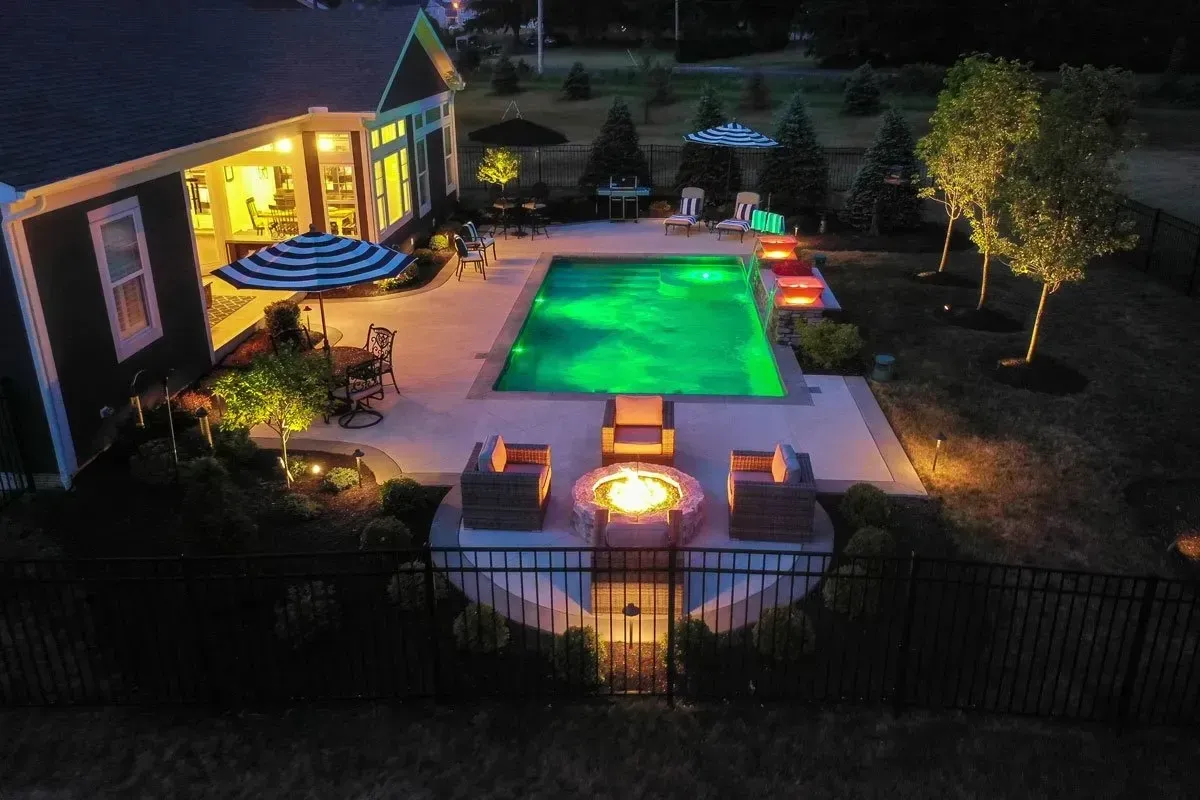 Luxury pool and travertine deck integrated with pavilion and outdoor kitchen on a Milton estate at dusk.