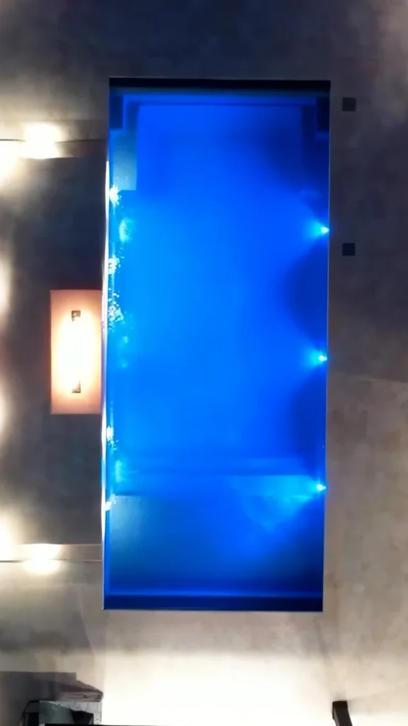 Nighttime vertical closeup of classical rectangle pool interior with ornate step design at shallow end lit LED blue — custom pool design and installation in Suwanee, GA by Primetime Pools.