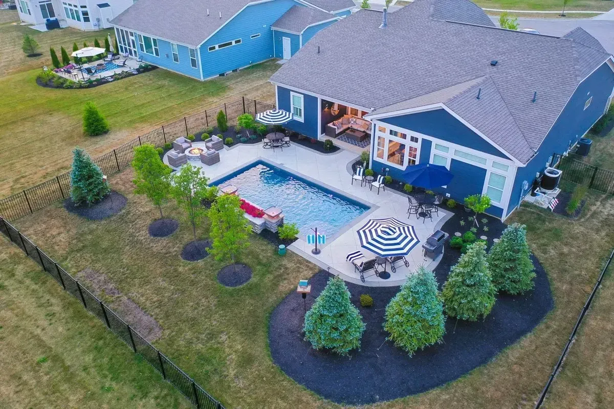 Aerial drone view of blue Cape Cod home in Laurel Springs Suwanee with rectangular pool, attached spa with spillover, and circular firepit