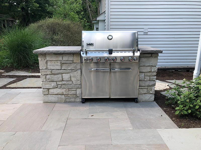 Weber Summit built-in gas grill on a single-bay stacked-stone island with flamed bluestone countertop on a gray bluestone running-bond patio in Forsyth County, GA