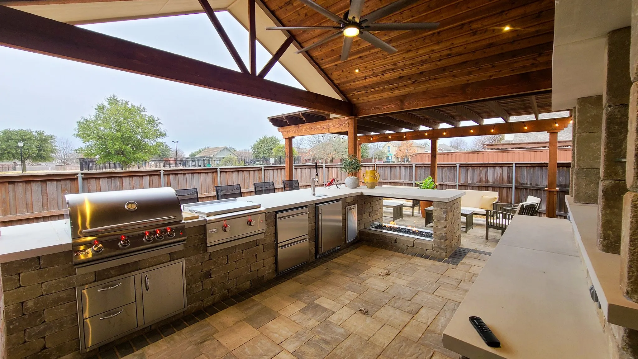 Large gable pavilion outdoor kitchen with cedar ceiling, ceiling fan, L-shape kitchen, bar seating, travertine patio, Forsyth County, GA