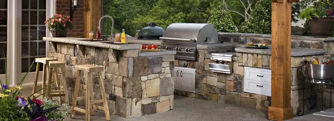 Rustic fieldstone L-shape outdoor kitchen with Big Green Egg, stainless grill, bar seating, and plumbed sink in Marietta, GA