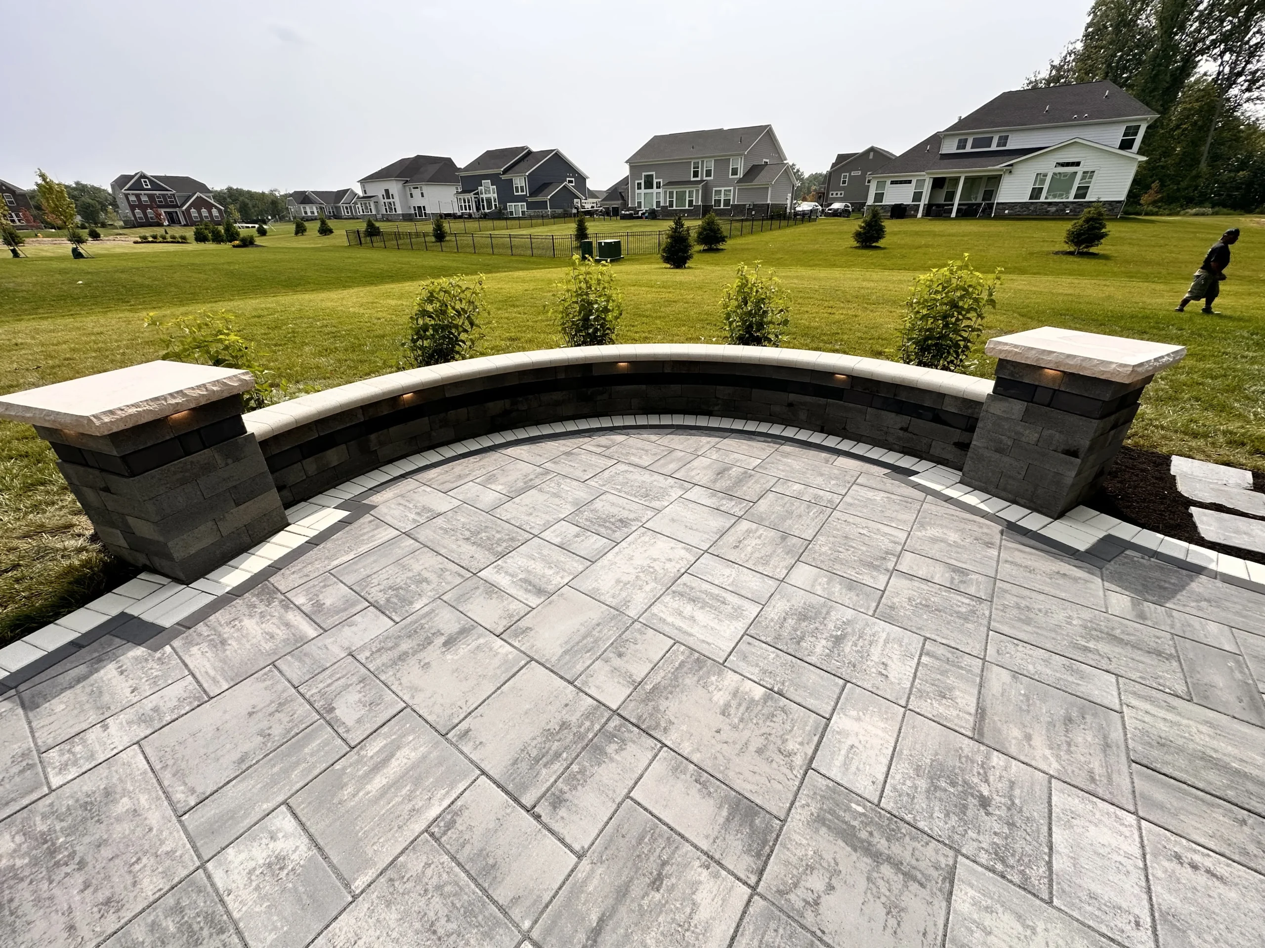 Large-format gray paver patio with raised seat wall and two stone column piers, overlooking open field — paver patio in Clarkston, GA by Primetime Pools.