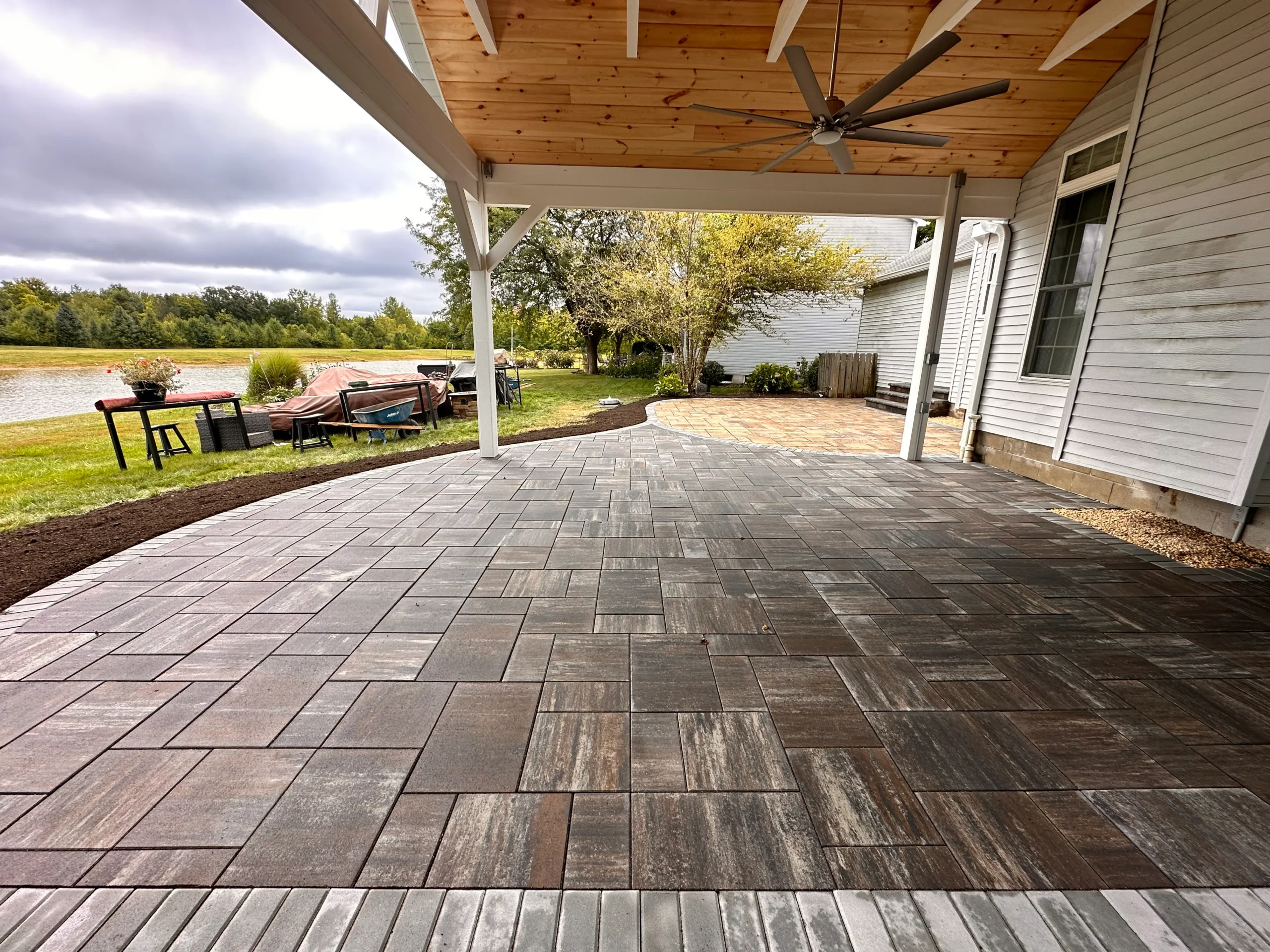 Warm brown plank-paver patio under attached covered porch, lake view, outdoor dining setup — paver patio in Clarkston, GA by Primetime Pools.