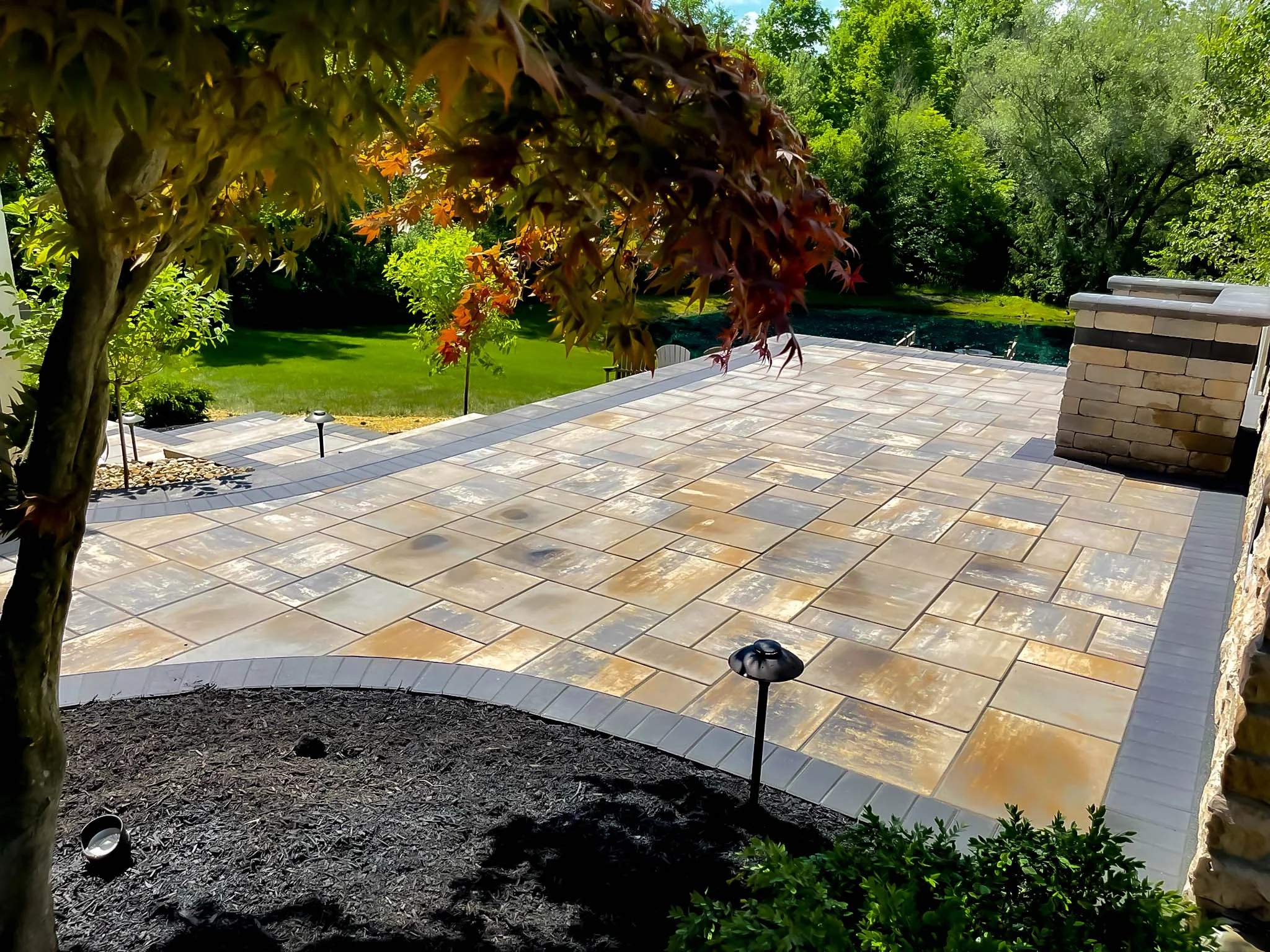 Curved natural flagstone patio with tan stacked stone seat wall and flowering trees, Dawsonville, GA