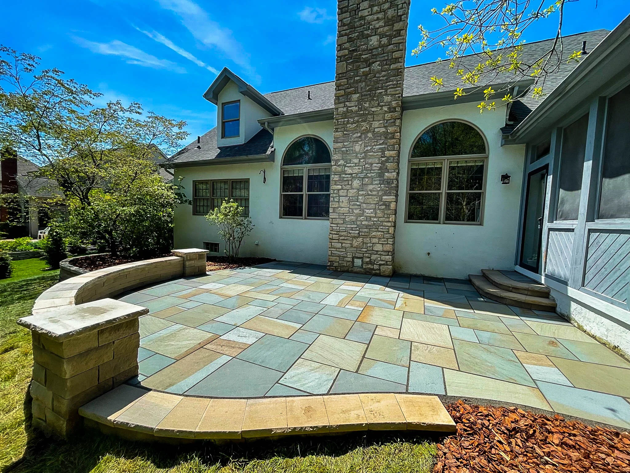 Two-level gray large-format paver patio with circular raised fire pit and cream-capped seat walls at a cream lap-siding home in Marietta, GA