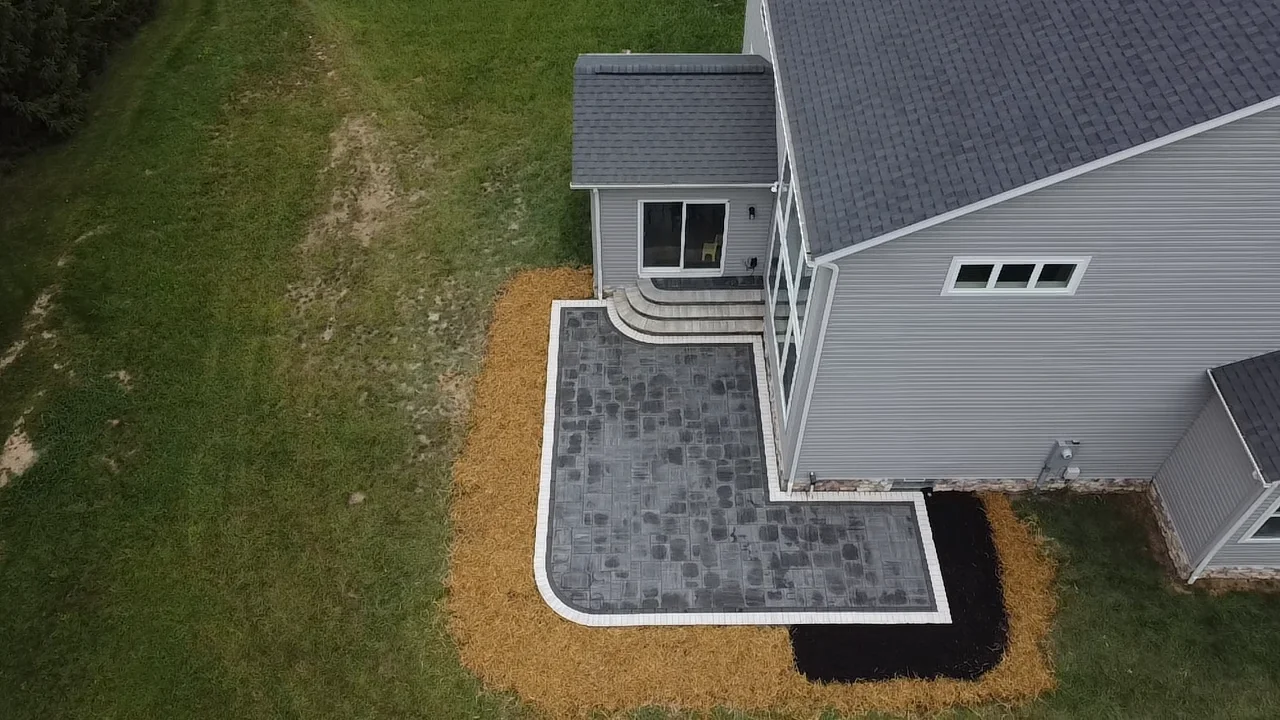 Aerial top-down view of a symmetric gray paver patio with twin curved seat-wall bump-outs and two stair sets on a new-build house in Suwanee, GA.