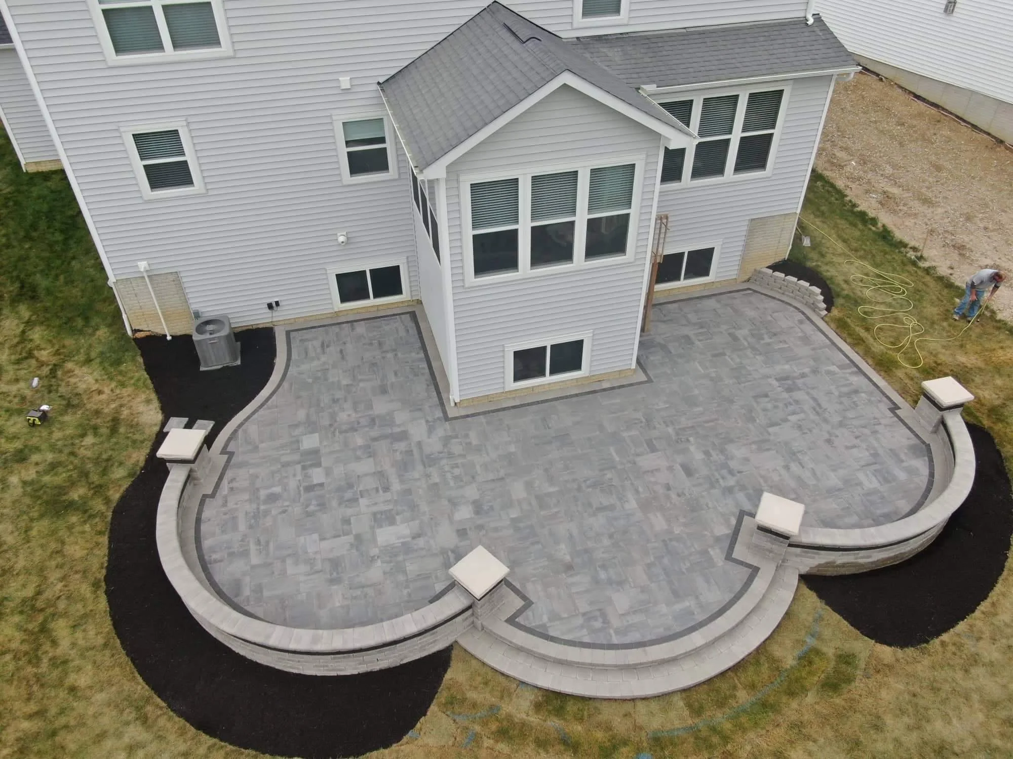Gray paver patio with curved seat wall, central fire pit, lantern-topped column piers, and fall foliage in Suwanee, GA.
