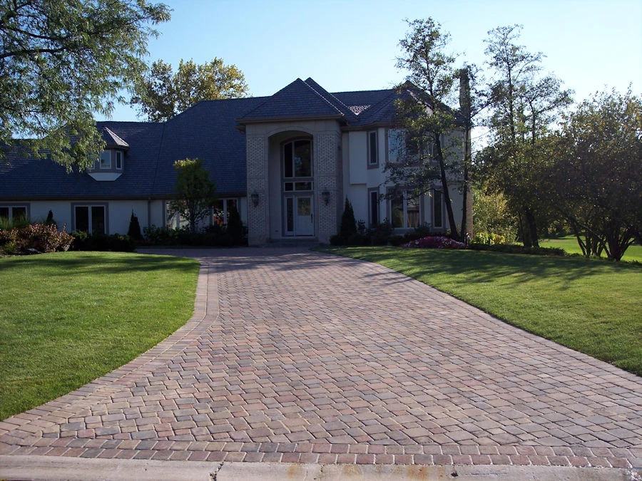 Long curving paver driveway in warm red/chestnut tones leading to a stately traditional home — paver hardscape in Clarkston, GA by Primetime Pools.