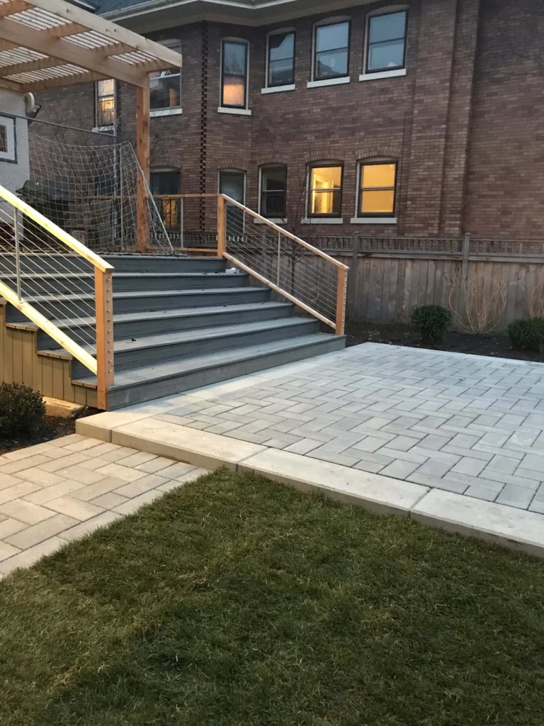 Elevated composite deck with cable-rail stairs dropping down to a fresh-install light-gray paver landing pad — paver hardscape in Cumming, GA by Primetime Pools.