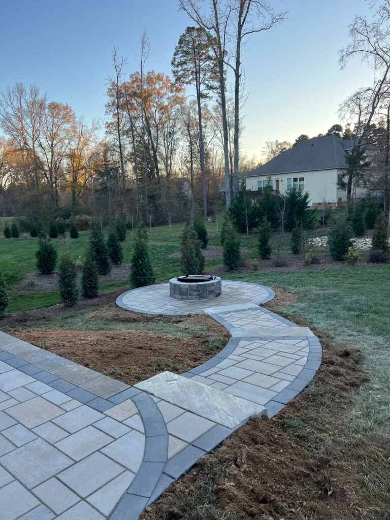 Curved paver walkway with sandlewood field and onyx soldier course leading past a circular firepit apron in Suwanee, GA