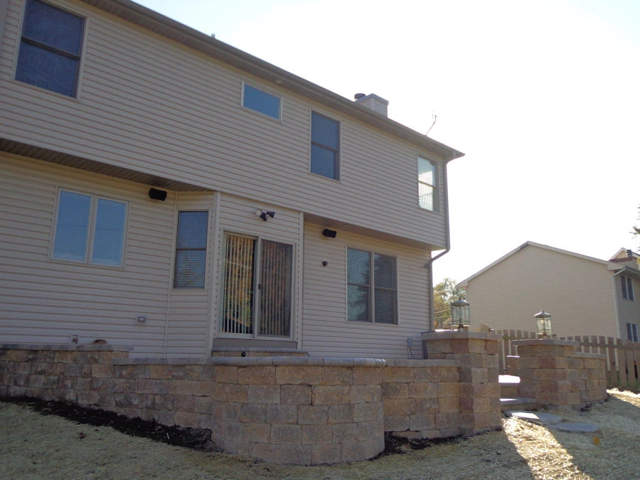 Tan segmental block retaining wall with dual lantern-topped column piers framing a raised back patio on a Dawsonville, GA new-build lot