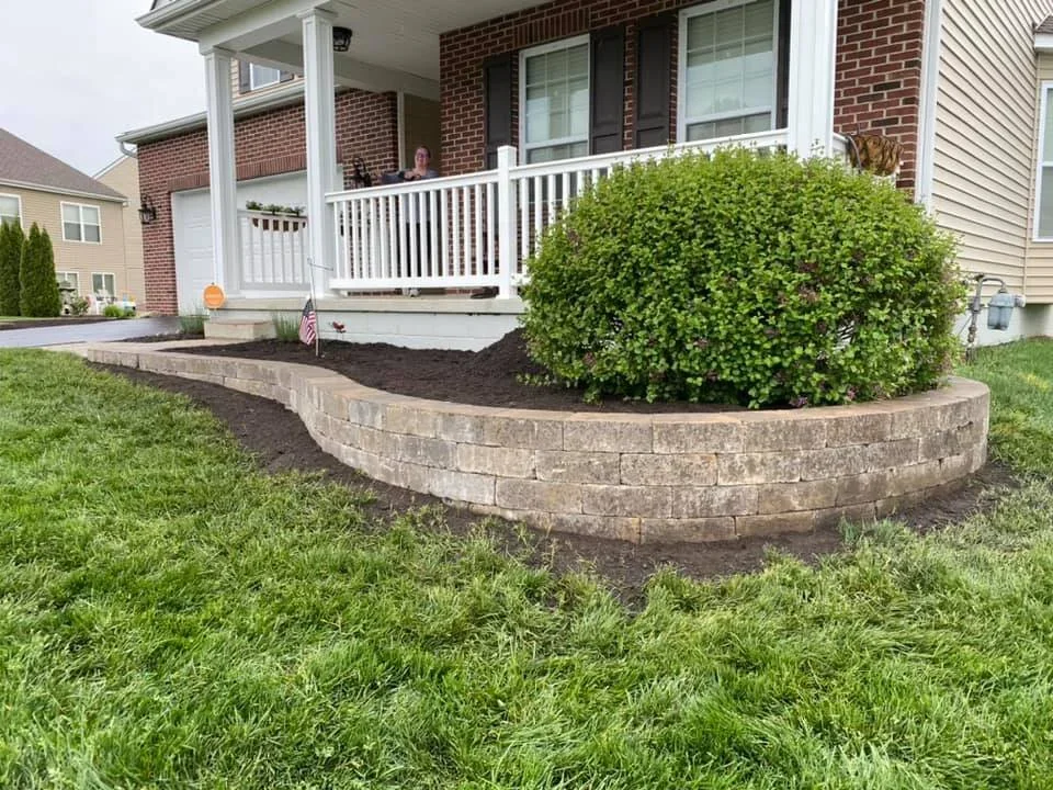 Curved low tan natural-ledgestone planter wall wrapping a ranch home corner with yellow flowers, Forsyth County, GA