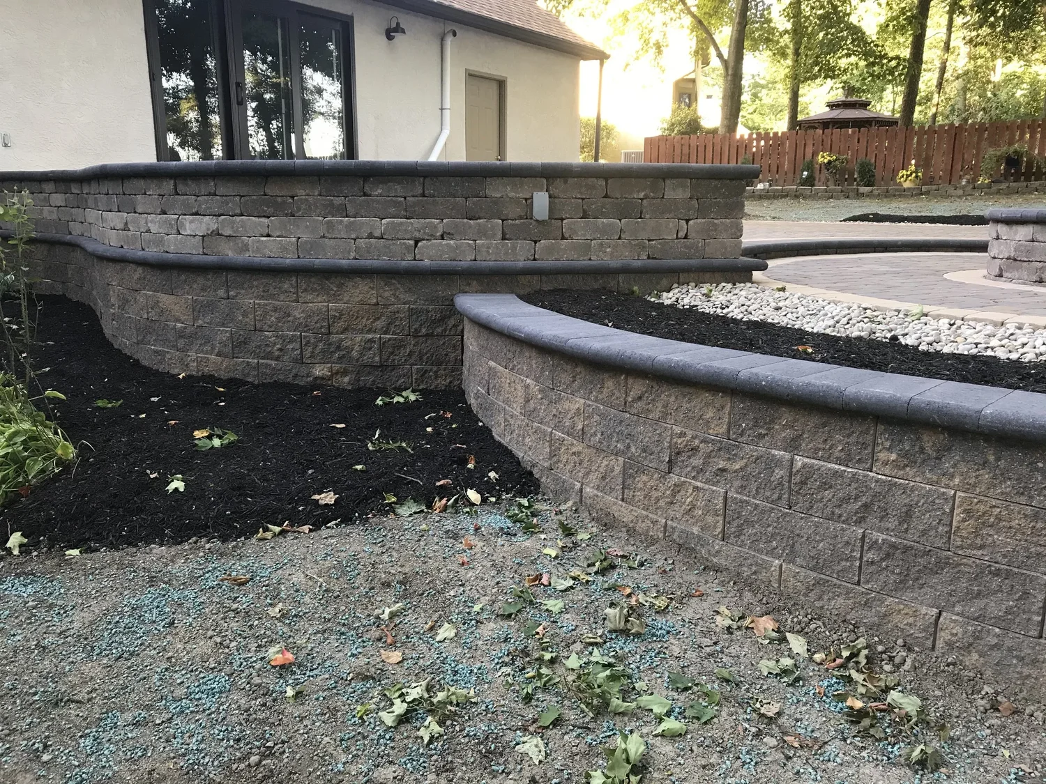 Two-tier charcoal segmental-block retaining wall with bullnose cap behind a cream stucco home in Forsyth County, GA