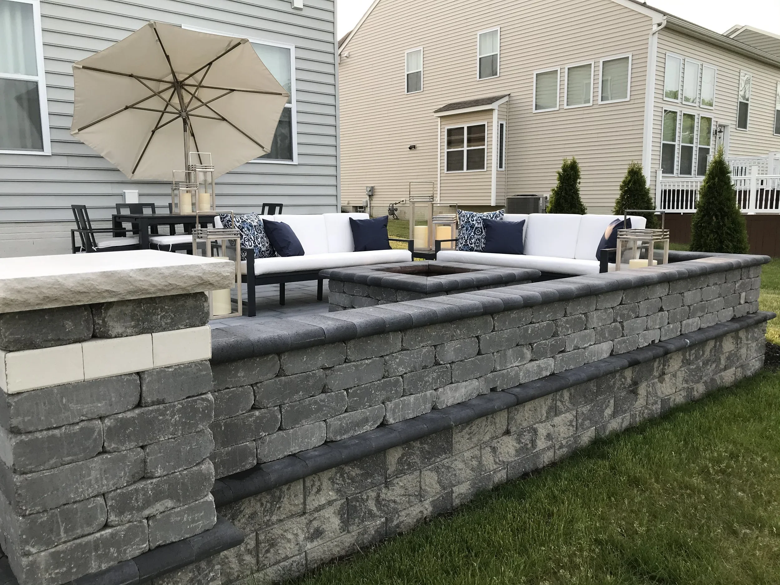 Long stacked-stone seat wall with paver cap wrapping a raised patio with outdoor furniture, farmhouse home in Forsyth County, GA