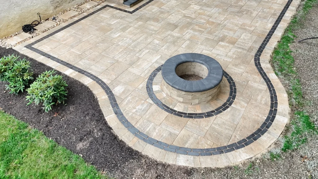 Curved tan paver patio with charcoal border and round stacked-stone firepit with dark coping ring — backyard firepit and fireplace in Alpharetta, GA by Primetime Pools.