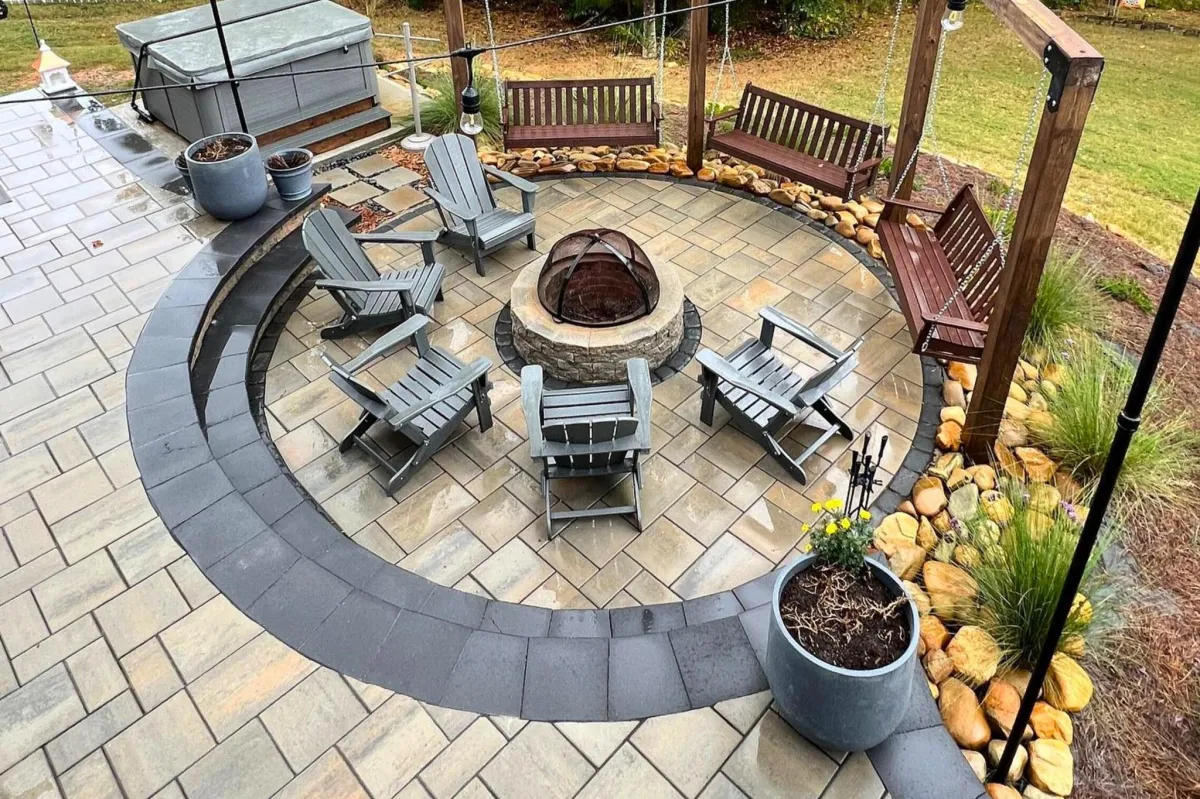 Integrated fire pit and fireplace hardscape in an Alpharetta, GA backyard with seating wall and paver surround