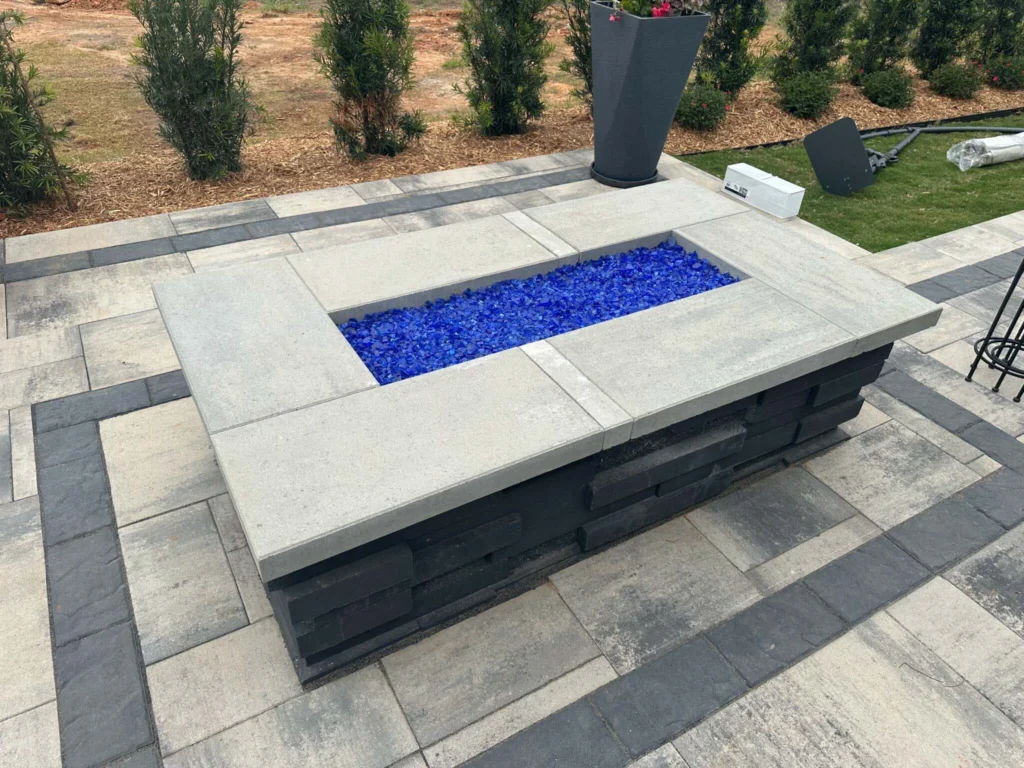 Ultra-modern rectangular gas firepit with bright cobalt blue fire glass and thick concrete cap on charcoal ledgestone base — backyard firepit and fireplace in Dacula, GA by Primetime Pools.
