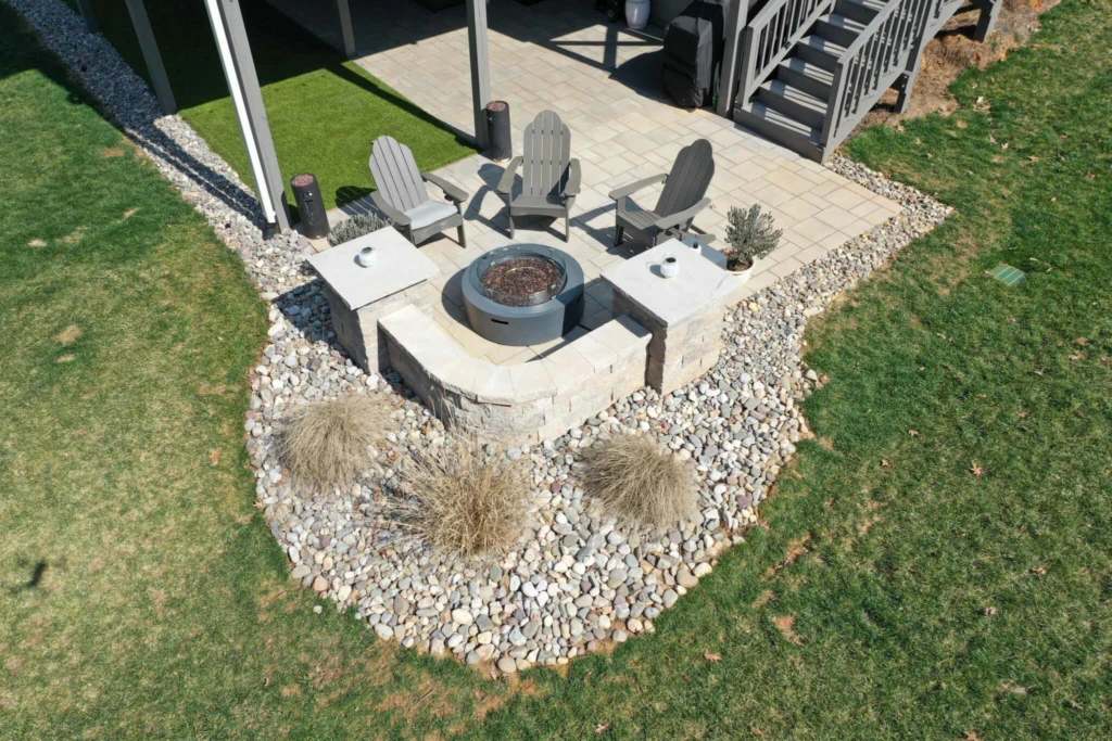 Corner firepit patio with raised pad, round gas firepit flanked by two square block-cap tables, stone surround — backyard firepit and fireplace in Forsyth County, GA by Primetime Pools.