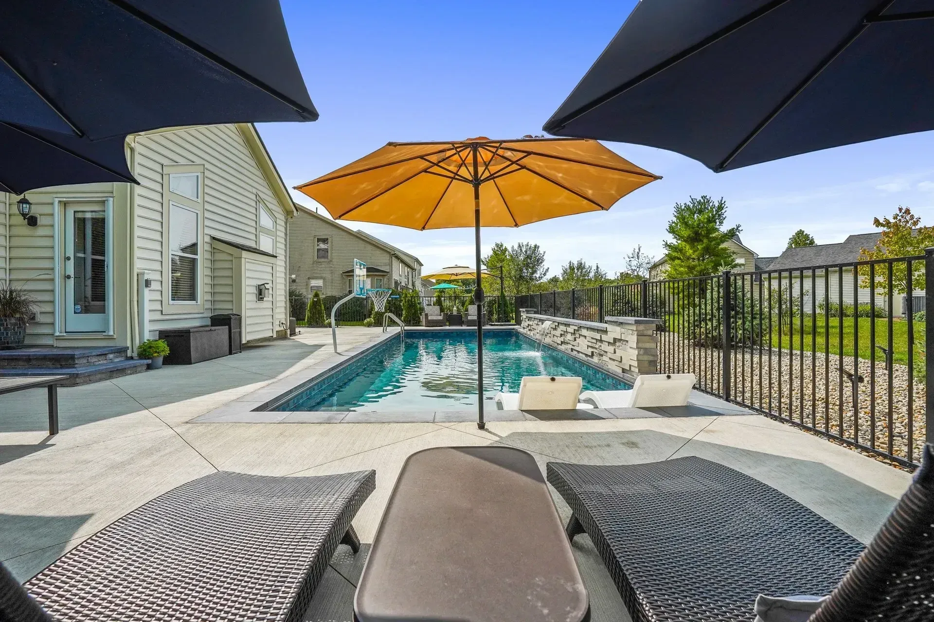 Rectangular Cumming pool with deck jets and cream tan tumbled paver deck around traditional brick home, Cumming GA