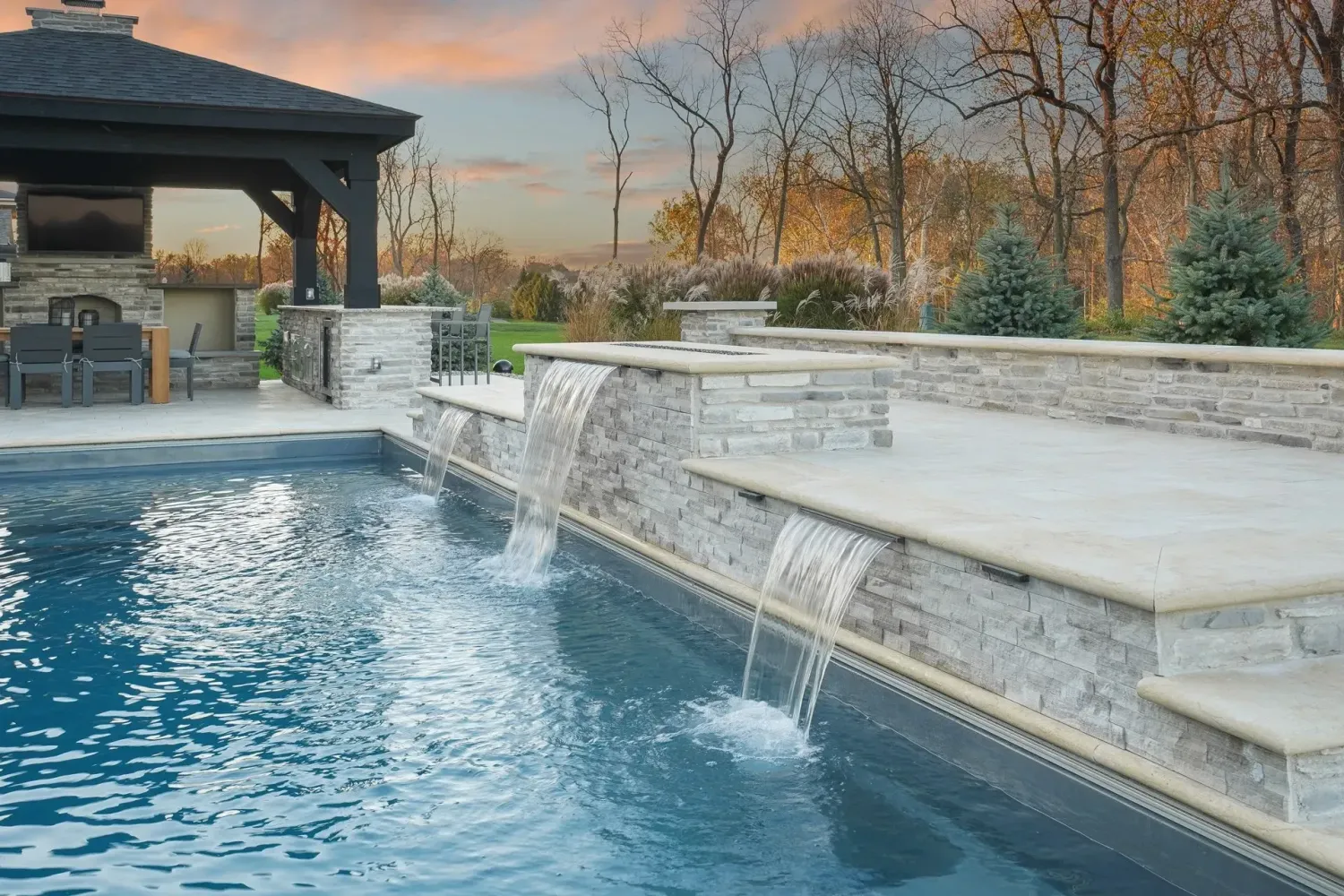 Rectangular pool with cream travertine deck and raised stacked-stone sheer-descent feature wall on a terraced Dawsonville, GA lot