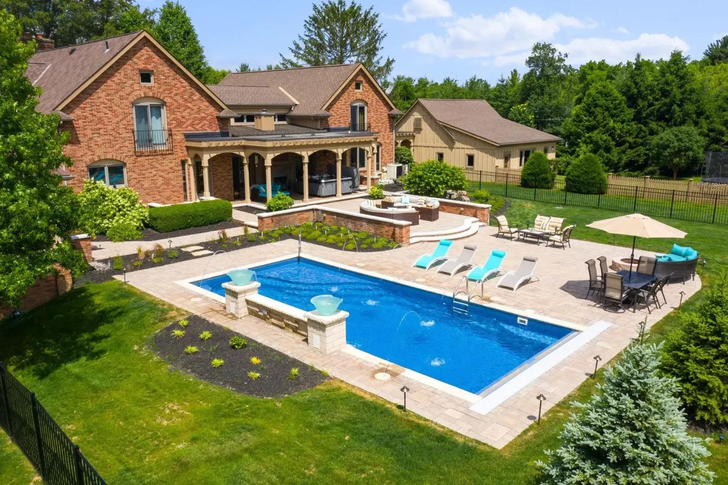 Traditional brick home backyard with rectangular pool, spa, tan paver deck with deck jets and raised planters in Suwanee, GA