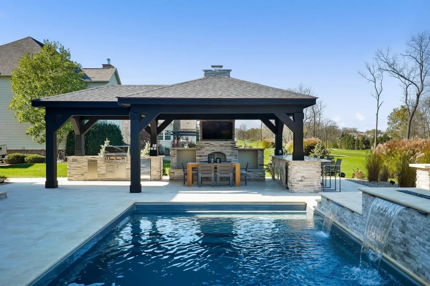 Black hip-roof pavilion over poolside outdoor kitchen with dark-liner pool and spa spillover in Cumming, GA