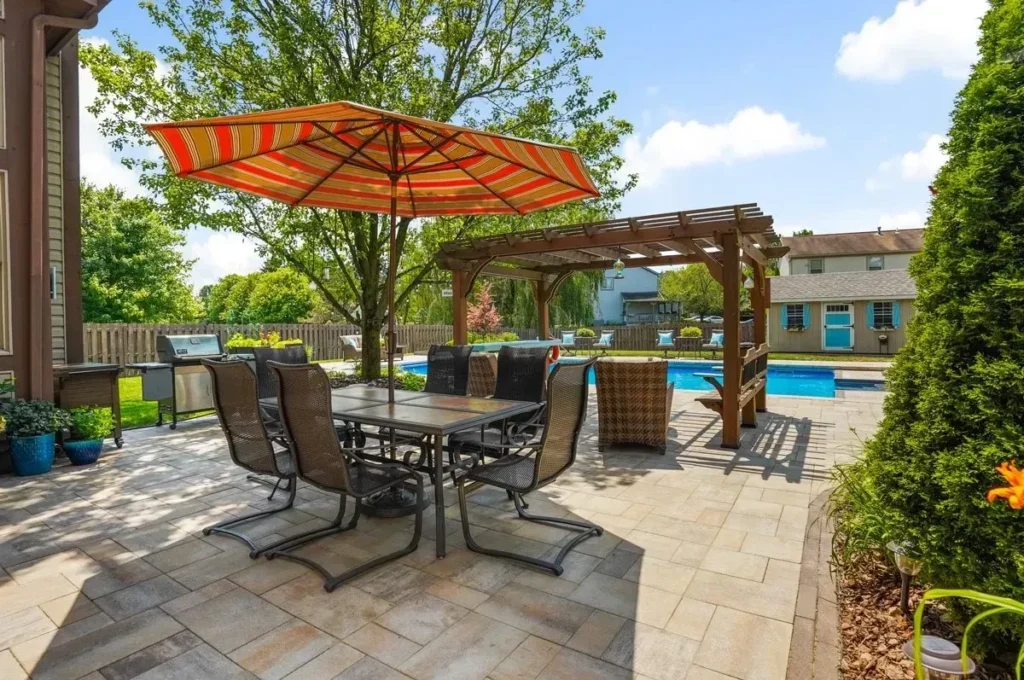 Cedar pergola over paver patio with orange patio umbrella, 6-chair dining set, pool in background — backyard pergola in Dacula, GA by Primetime Pools.