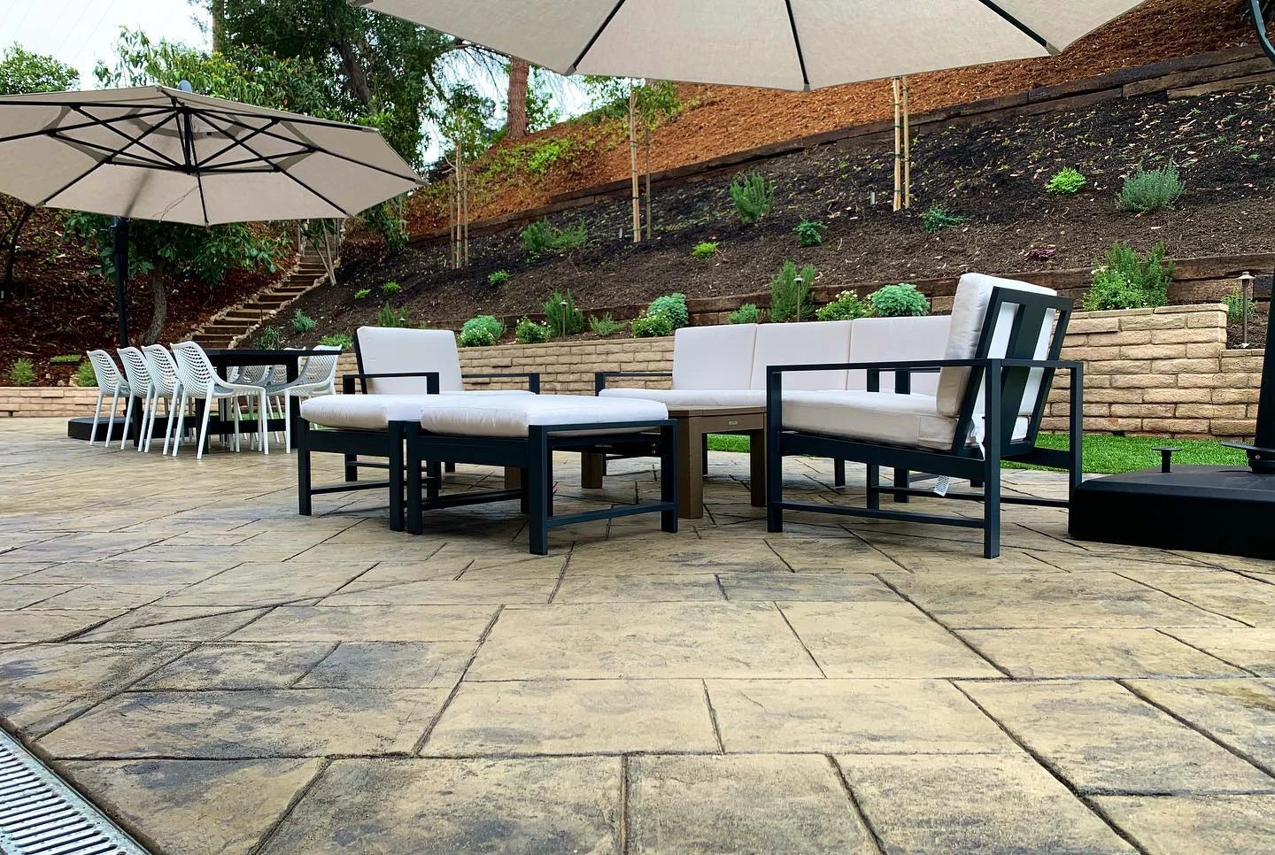 Sloped Forsyth County backyard with stamped concrete patio, tiered split-face retaining wall garden and modern black sectional seating